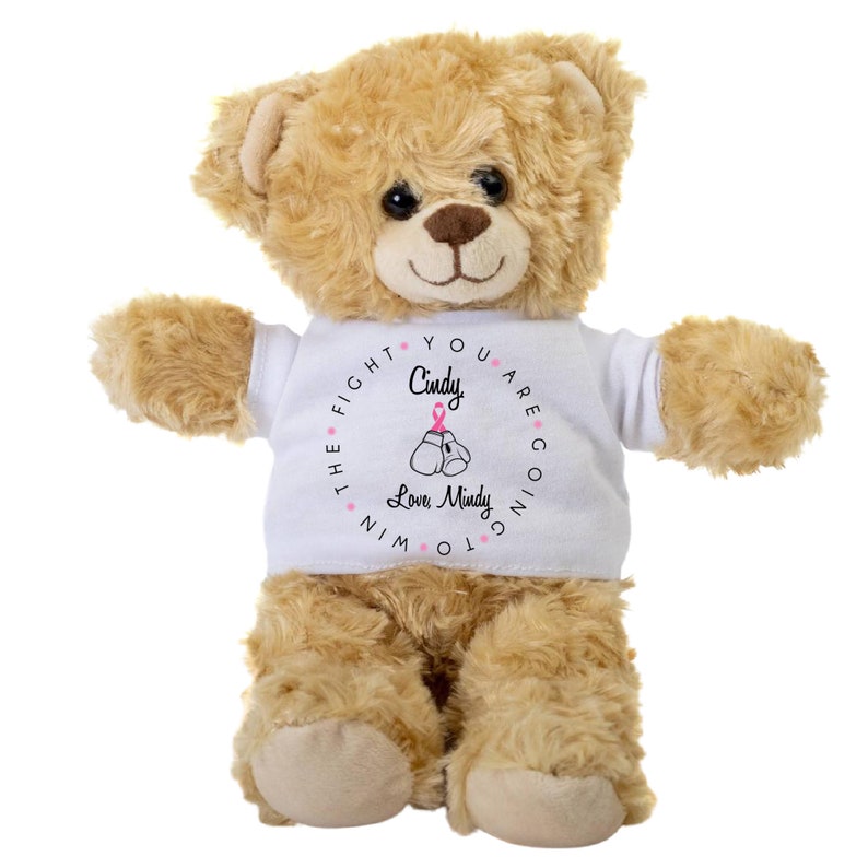May include: A tan teddy bear wearing a white t-shirt with a pink ribbon and boxing gloves graphic. The shirt says "You are going to win the fight. Cindy. Love Mindy."
