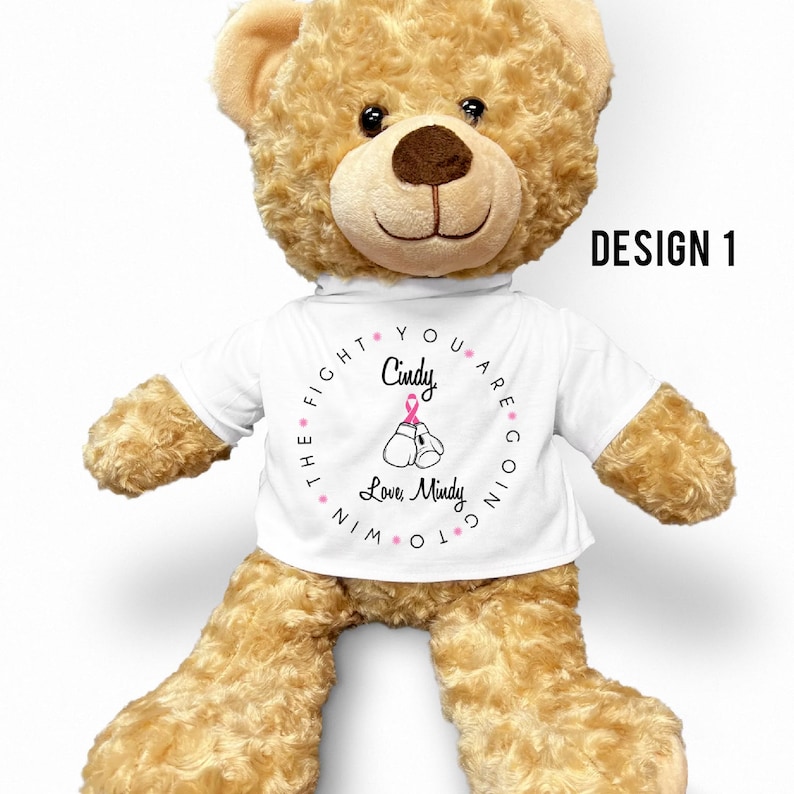 May include: A brown teddy bear wearing a white t-shirt with the text "You are going to win the fight. Cindy Love, Mindy" and a pink ribbon on boxing gloves.