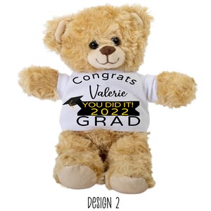 Puede incluir: Un oso de peluche marr&oacute;n que lleva una camiseta blanca con el texto "Congrats Valerie You Did It! 2022 Grad" en negro y amarillo. La camiseta tiene un gr&aacute;fico de gorro de graduaci&oacute;n negro.