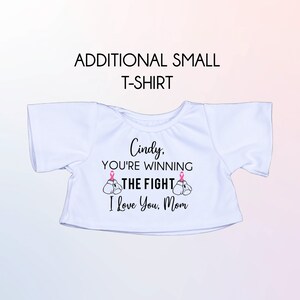 May include: White t-shirt with a pink ribbon design and the text "Cindy, You're Winning The Fight I Love You, Mom".