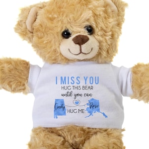 May include: A tan teddy bear wearing a white t-shirt with the text "I MISS YOU". The shirt includes blue state outlines of Alabama and Alaska, with the names "Cindy" and "Rosie" connected by a heart, and the words "HUG ME".