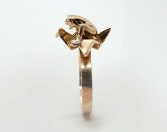 May include: A gold ring with a small origami crane and a frog sitting on top of it.