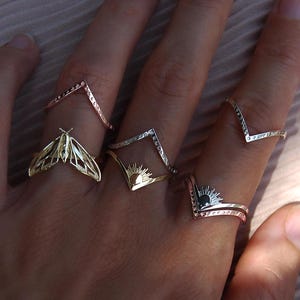 May include: A set of four gold rings with different designs. One ring features a butterfly, another has a sun, and the other two are simple geometric shapes.