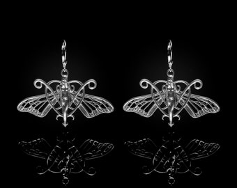 May include: A pair of silver earrings featuring a delicate butterfly design with a stylized human figure in the center. The earrings are suspended from a simple hoop.