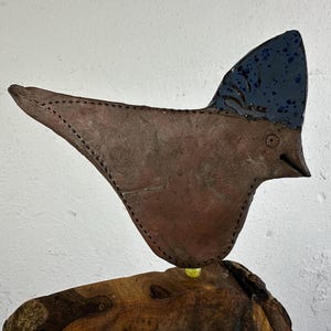 Könnte beinhalten: Handgefertigte Keramik-Vogelskulptur mit braunem Körper und dunkelblauem Kamm. Der Vogel hat einen spitzen Schnabel und ist auf einem Holzstück montiert. Die Skulptur ist ein einzigartiges Kunstwerk.