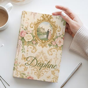 May include: A book with a floral design and the name "Daphne" in script. The cover has a framed image of a couple and a house, surrounded by roses and butterflies. A white mug with coffee and a pen are also visible.