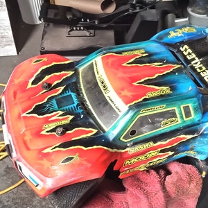 May include: A red, blue, and black remote control truck with the words "WRRECKLESS" and "SXT" on the side. The truck has a black and yellow flame design on the hood.