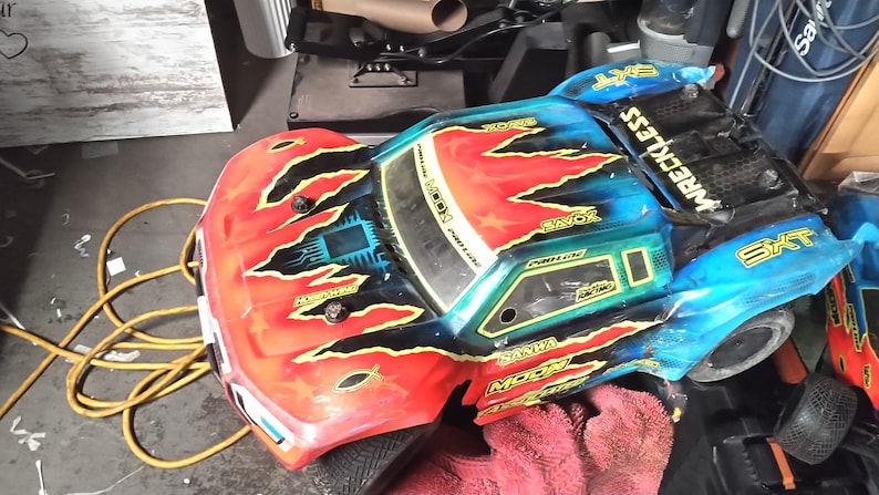 May include: A red, blue, and black remote control truck with the words "WRRECKLESS" and "SXT" on the side. The truck has a black and yellow flame design on the hood.