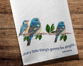 May include: A white tea towel with a watercolor painting of three blue birds perched on a branch with green leaves. The text "...every little thing's gonna be alright... Bob Marley" is printed below the birds.