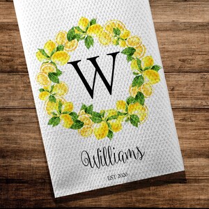 May include: White kitchen towel with a lemon wreath design. The wreath surrounds a large black letter "W". The word "Williams" is written in script below the letter, with "EST 2020" underneath.