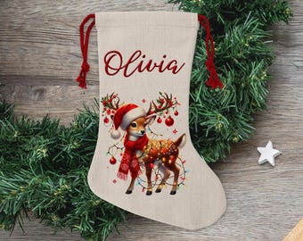 May include: Personalized Christmas stocking with a white background and a red and white reindeer with lights and ornaments. The stocking has the name "Olivia" embroidered on it.