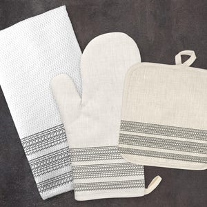 May include: A set of three kitchen textiles in a cream color with black trim. The set includes a potholder, an oven mitt, and a tea towel. All three items feature a black embroidered design of repeating circles.