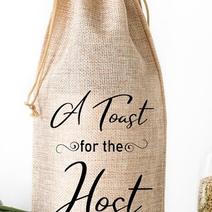 Może przedstawiać: Brązowa torba na butelkę wina z juty ze sznurkiem do ściągania. Torba ma nadrukowany napis "A Toast for the Host".
