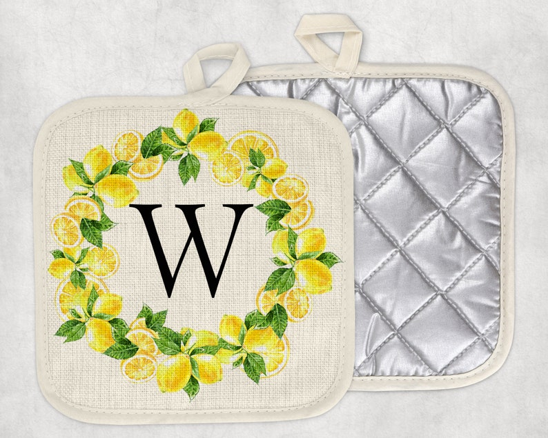 May include: Two square pot holders. One features a lemon wreath design with the letter "W" in the center. The other has a quilted silver lining. Both have a loop for hanging. The pot holders are cream-colored.