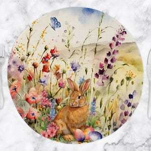 May include: Round placemat with a watercolor design featuring a brown rabbit, colorful flowers, and Easter eggs. A blue butterfly flutters above the rabbit. The placemat is surrounded by a fork and knife.