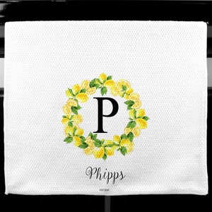 May include: White kitchen towel with a lemon wreath design. The wreath surrounds a large black letter "P". The name "Phipps" is written in cursive below the wreath, with "EST 2020" below the name.
