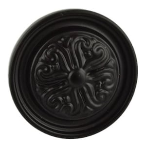 May include: Black metal knob with a decorative, ornate design. The knob has a raised, circular center and a surrounding ring.