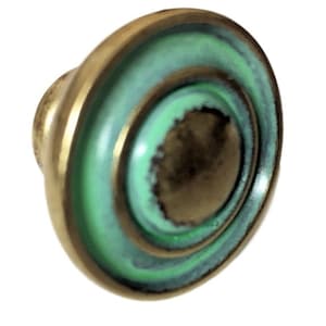 May include: A green and gold round cabinet knob with a raised center and concentric circles.