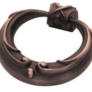 May include: A decorative ring pull cabinet handle with a brushed antique copper finish. The handle features a swirling, ornate design.