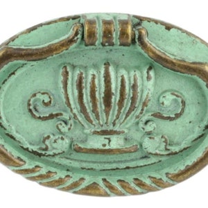 May include: Oval-shaped cabinet pull with a distressed, aged appearance. The pull features a light teal base with bronze-colored accents. The design includes a central vase motif and decorative scrollwork, suitable for furniture restoration or decorative projects.
