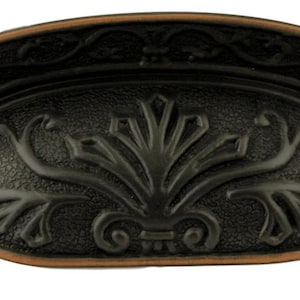 May include: A black and copper cabinet pull with an ornate design. The pull is shaped like a half-circle and has a raised floral pattern.