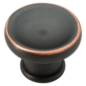 May include: A round, black cabinet knob with a copper accent around the edge. The knob has a slightly raised, rounded top.