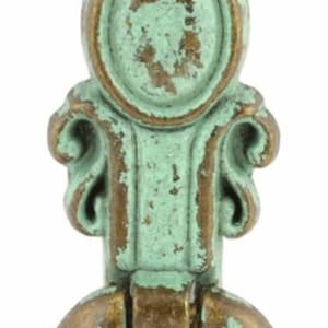 May include: A green and gold metal door knocker with an ornate design. The knocker has a ring-shaped handle and a decorative top.