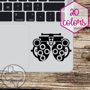 May include: Black and white silhouette of an eye chart with multiple circles and a horizontal bar at the top. The image is on a silver laptop.