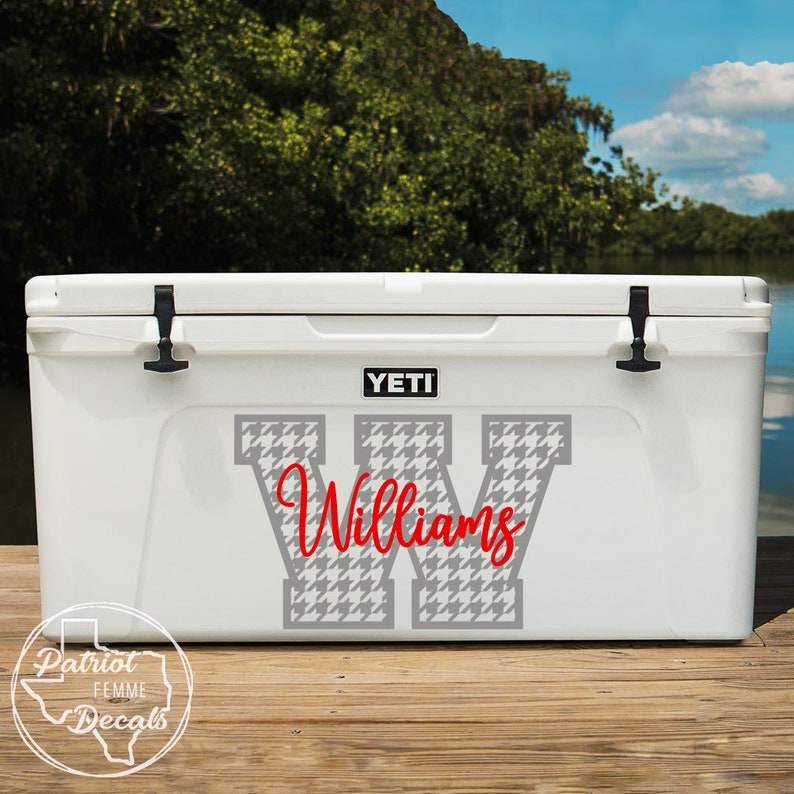 Op de afbeelding: Witte YETI-koeler met zwarte grendels en het woord "YETI" in zwart. De koeler is versierd met een grote grijze letter "W" in een hondenpootpatroon en de naam "Williams" in rood script.