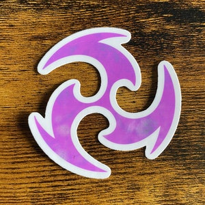 May include: A purple and white sticker with a three-pointed star design. The star is stylized with a swirling, organic shape.