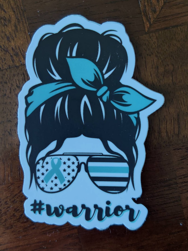 Puede incluir: Una pegatina con una silueta negra de una mujer con un mo&ntilde;o desordenado, que lleva gafas de sol con una cinta azul y un fino patr&oacute;n de rayas azules y blancas. El texto "#warrior" est&aacute; debajo de las gafas de sol.
