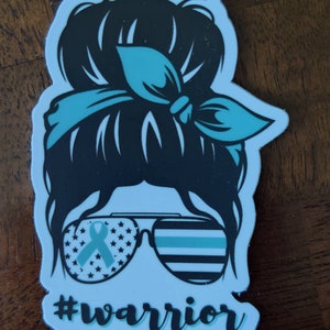 Puede incluir: Una pegatina con una silueta negra de una mujer con un mo&ntilde;o desordenado, que lleva gafas de sol con una cinta azul y un patr&oacute;n a rayas azul y blanco. El texto "#warrior" est&aacute; debajo de las gafas de sol.
