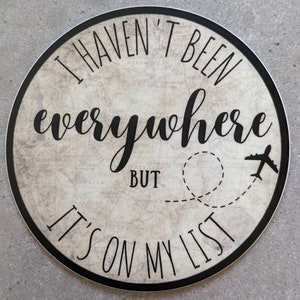 May include: A round sticker with a vintage map background. The sticker features the text "I haven't been everywhere but it's on my list" with a plane and a dotted line representing a flight path.