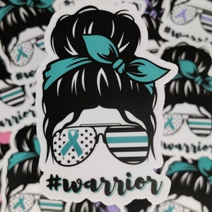 Puede incluir: Una pegatina con una imagen de dibujos animados de una mujer con un mo&ntilde;o desordenado, que lleva gafas de sol con una cinta turquesa y una cinta turquesa atada alrededor de su mo&ntilde;o. Las gafas de sol tienen una fina l&iacute;nea azul y estrellas en las lentes. El texto '#warrior' est&aacute; debajo de la imagen.