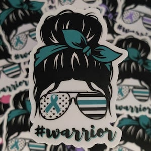 Puede incluir: Una pegatina con una ilustraci&oacute;n de dibujos animados de una mujer con un mo&ntilde;o desordenado, que lleva gafas de sol con una bandera estadounidense y una cinta turquesa. Las gafas de sol tambi&eacute;n tienen una fina l&iacute;nea azul en la parte superior. El texto "#warrior" est&aacute; debajo de la imagen.