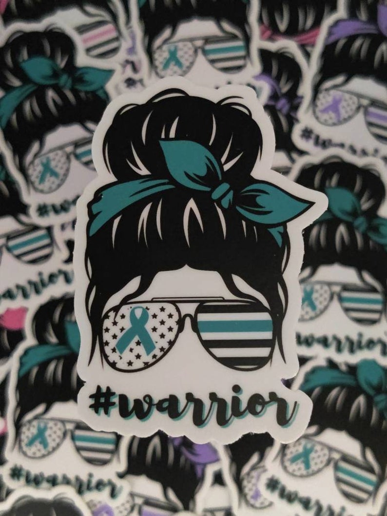 Puede incluir: Una pegatina con una ilustraci&oacute;n de dibujos animados de una mujer con un mo&ntilde;o desordenado, que lleva gafas de sol con una bandera estadounidense y una cinta turquesa. Las gafas de sol tambi&eacute;n tienen una fina l&iacute;nea azul en la parte superior. El texto "#warrior" est&aacute; debajo de la imagen.