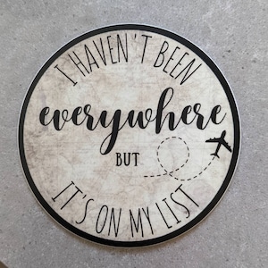 May include: Round sticker with a vintage map background. The sticker says "I haven't been everywhere but it's on my list" with a plane and a dotted line representing a flight path.