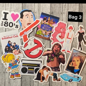 May include: A collection of 10 colorful stickers featuring various 80s pop culture icons, including The Breakfast Club, Ghostbusters, Care Bears, and a boombox. The stickers are on a wooden background.
