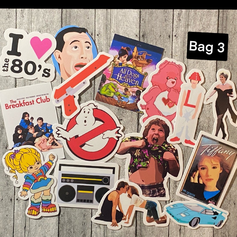 May include: A collection of 10 colorful stickers featuring various 80s pop culture icons, including The Breakfast Club, Ghostbusters, Care Bears, and a boombox. The stickers are on a wooden background.