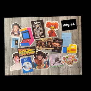 May include: A collection of vintage stickers featuring characters and movie titles from the 1980s, including "Back to the Future", "E.T.", "Clue", "London Calling", "A Brief History of Time", and "The Muppet Babies".