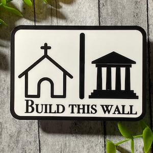 May include: Black and white sticker with a church, a wall, and a building with columns. The text "BUILD THIS WALL" is below the images.