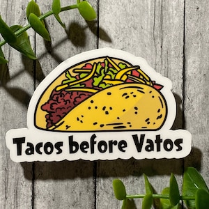 Op de afbeelding: Witte sticker met een cartoontekening van een taco met de tekst "Tacos before Vatos" in zwart.