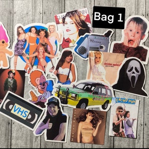 Puede incluir: Una colecci&oacute;n de 15 pegatinas vintage con varios iconos de la cultura pop y temas de los a&ntilde;os 90. Las pegatinas incluyen im&aacute;genes de Shania Twain, Christina Aguilera, un mu&ntilde;eco troll, una cinta VHS, un Jeep, una m&aacute;scara de Scream y una escena de la pel&iacute;cula 'Encino Man'. Las pegatinas est&aacute;n todas sobre un fondo de madera.