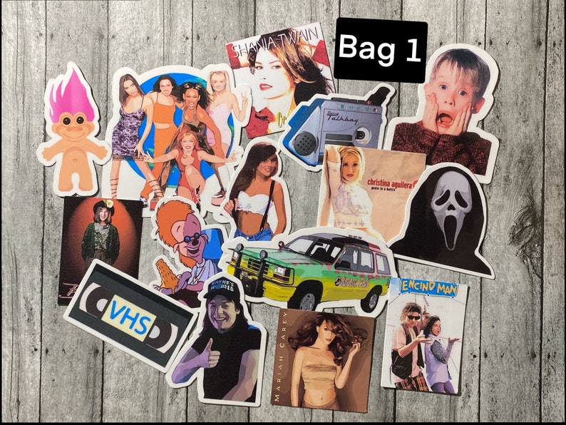 Puede incluir: Una colecci&oacute;n de 15 pegatinas vintage con varios iconos de la cultura pop y temas de los a&ntilde;os 90. Las pegatinas incluyen im&aacute;genes de Shania Twain, Christina Aguilera, un mu&ntilde;eco troll, una cinta VHS, un Jeep, una m&aacute;scara de Scream y una escena de la pel&iacute;cula 'Encino Man'. Las pegatinas est&aacute;n todas sobre un fondo de madera.