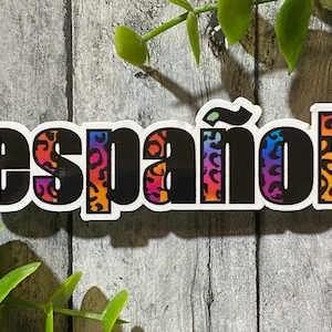 Op de afbeelding: Een sticker met het woord "español" in zwarte blokletters. De letters hebben een luipaardprint in oranje, roze, paars en blauw. De sticker heeft een witte rand.