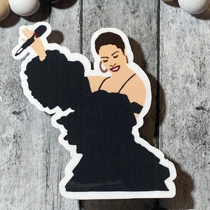 Op de afbeelding: Een zwart-witte illustratie van een vrouw die in een microfoon zingt. Ze draagt een zwarte jurk met een grote ruche op de schouder. De achtergrond is een houten oppervlak.
