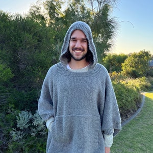 Pode incluir: Um poncho cinza com capuz e um grande bolso na frente. O poncho é feito de um tecido macio e de malha.