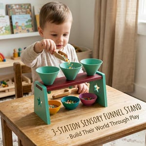 May include: A wooden sensory funnel stand featuring three teal funnels mounted on a dark red horizontal bar with teal side supports, each with a star cutout. Includes three small bowls in yellow, teal, and purple, plus two wooden scoops.