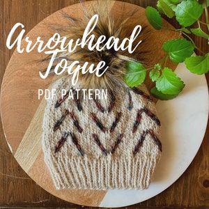 May include: A knitted beanie with an arrowhead design in shades of beige, brown, and red. The hat features a faux fur pom-pom and the text "Arrowhead Toque PDF Pattern" in a script font.