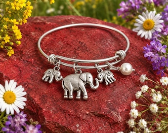 May include: A silver-toned bangle bracelet featuring three dangling elephant charms of varying sizes and a single white pearl bead. The metal charms have a textured, antique finish and are attached to the circular wire band by small metal loops.